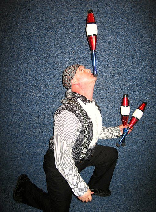 A man is juggling two clubs in his mouth
