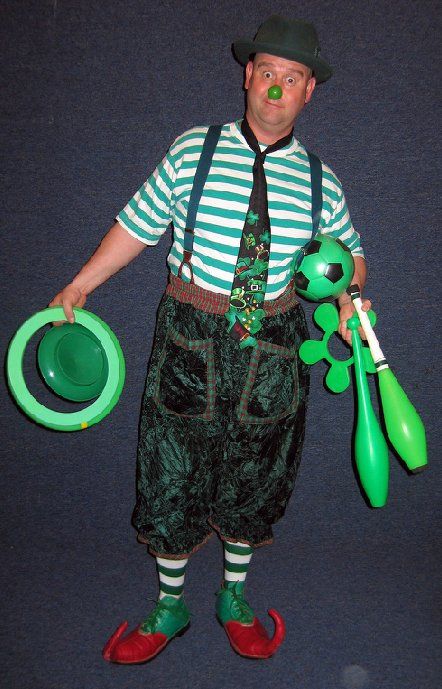 A man dressed as a clown is holding balloons and juggling clubs