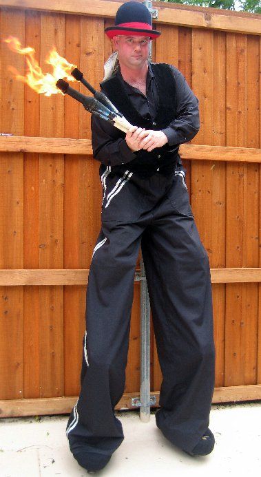 A man is standing on stilts holding a fire stick.