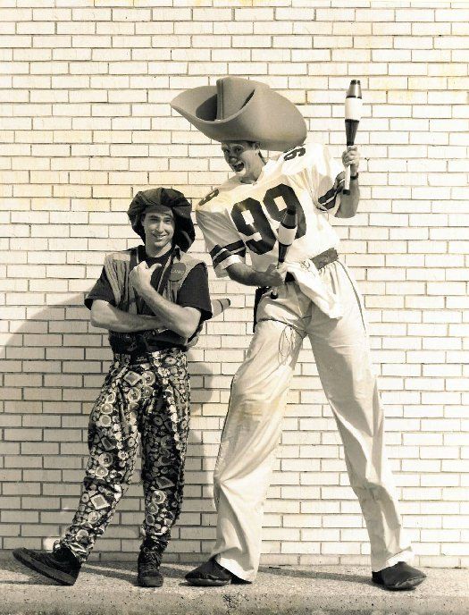A man in a number 99 jersey stands next to a man on stilts