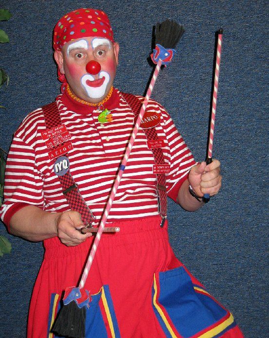 A man dressed as a clown is holding a broom