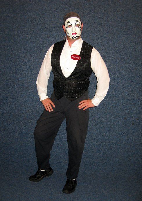A man wearing a white mask and a black vest is standing with his hands on his hips