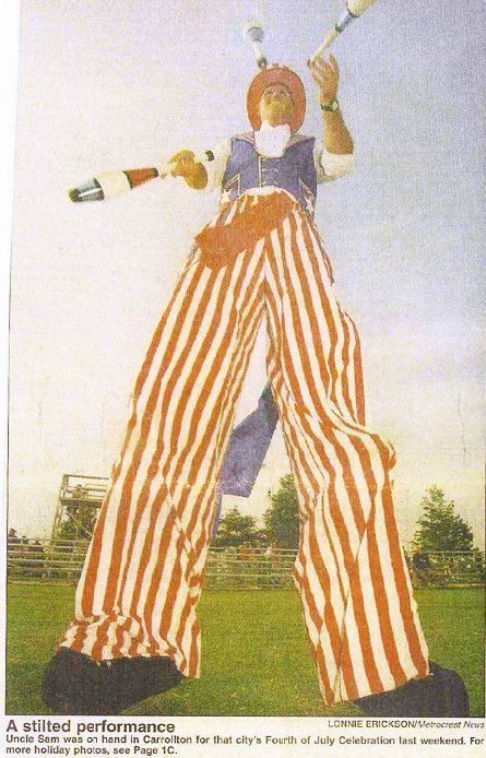 A clown on stilts is holding a baseball bat