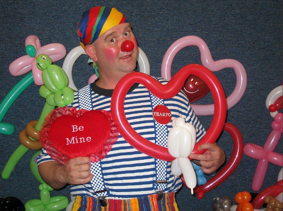 A clown is holding a red heart that says be mine