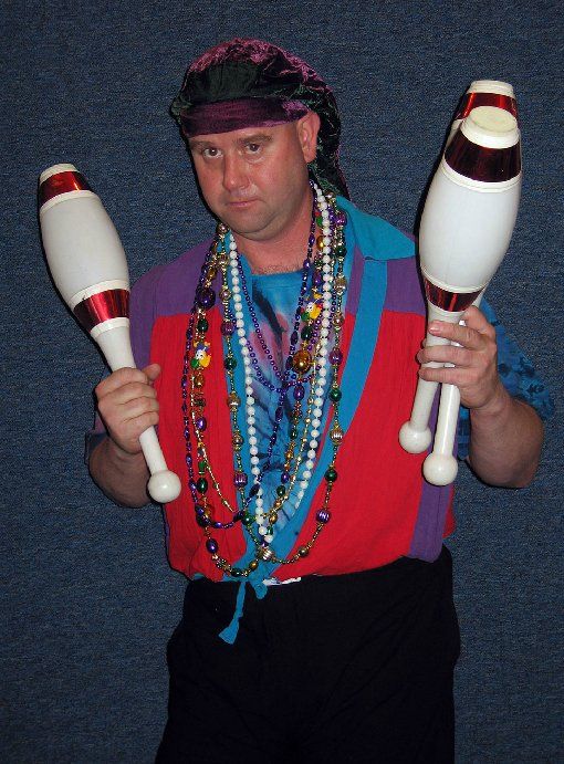 A man with beads around his neck is holding two juggling pins