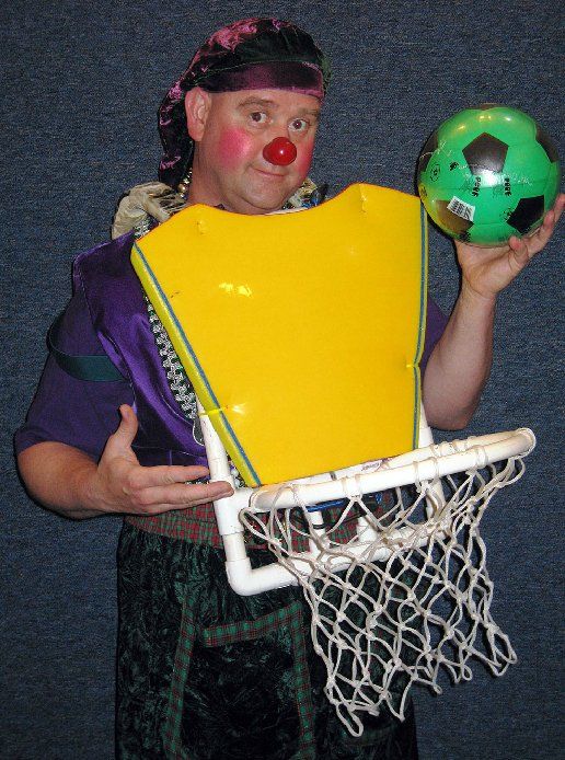 A man in a clown costume is holding a soccer ball and a basketball net