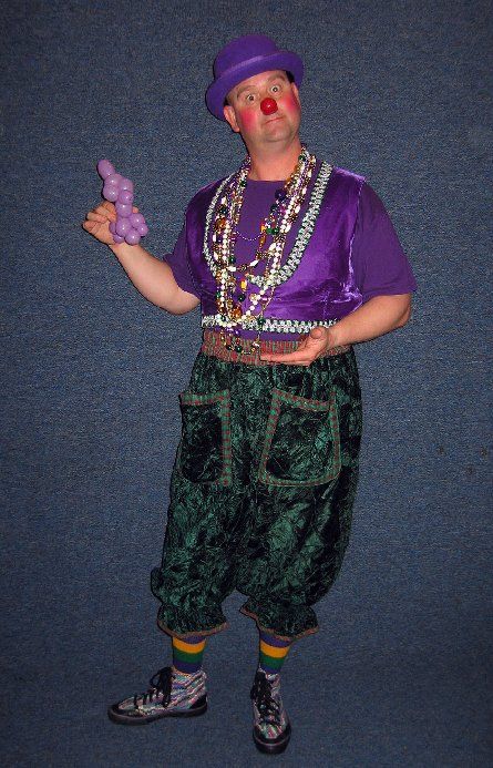 A man dressed as a clown is holding a bunch of balloons.