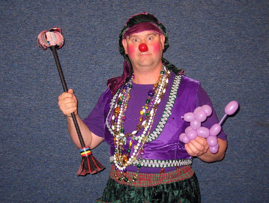 A man dressed as a clown is holding balloons and a mop