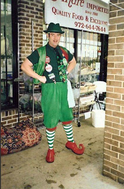 A man dressed as an elf is standing in front of a sign that says quality food & excellent