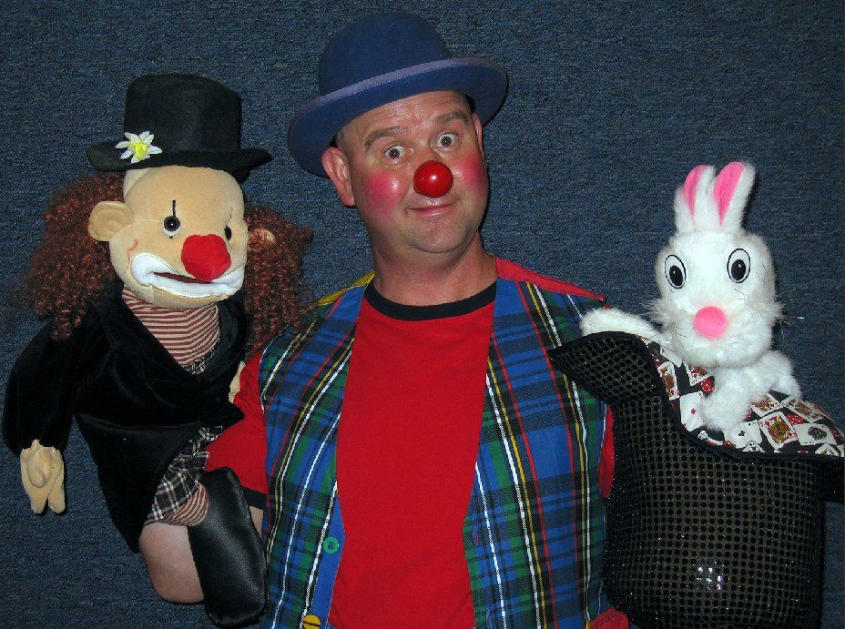 A man in a clown costume is holding two stuffed animals