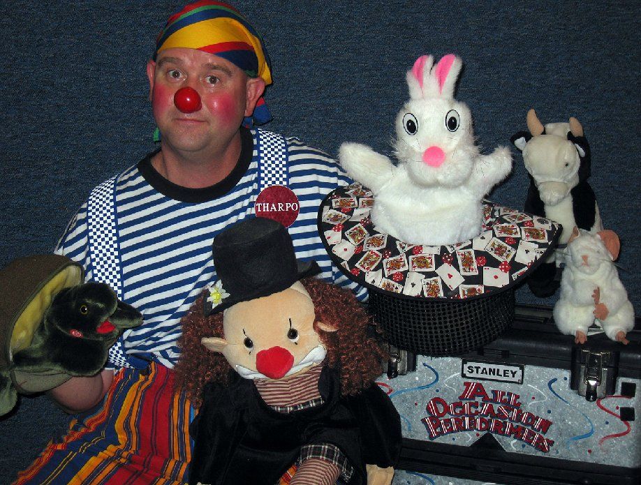 A man in a clown costume is surrounded by stuffed animals