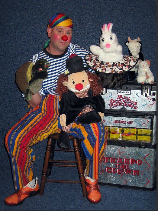 A man in a clown costume is sitting on a stool with stuffed animals