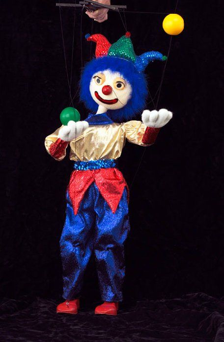 A clown puppet is holding a yellow ball and a green ball.