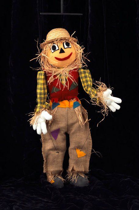 A scarecrow with a straw hat and gloves is standing on a black background.