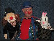 A man in a clown costume is standing next to two stuffed animals.