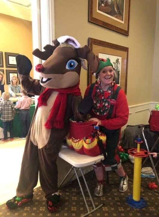 A woman in an elf costume stands next to a reindeer mascot