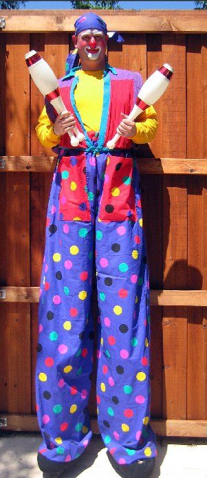 A clown on stilts is holding two juggling pins