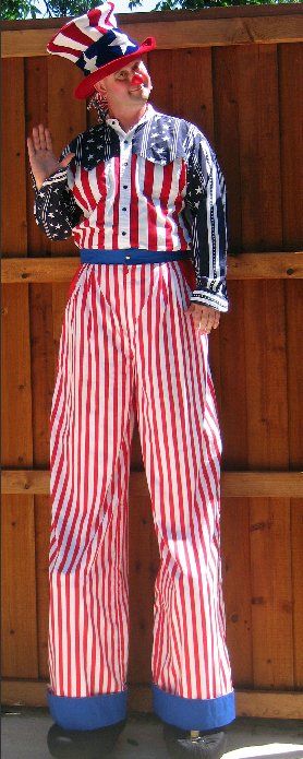 A man in an uncle sam costume is standing on stilts in front of a wooden fence.
