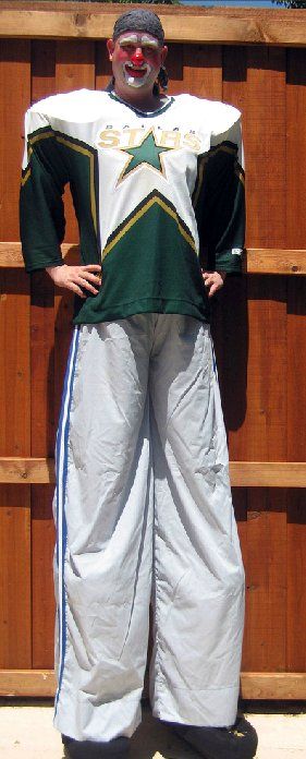 A man on stilts is wearing a green and white jersey with a star on it