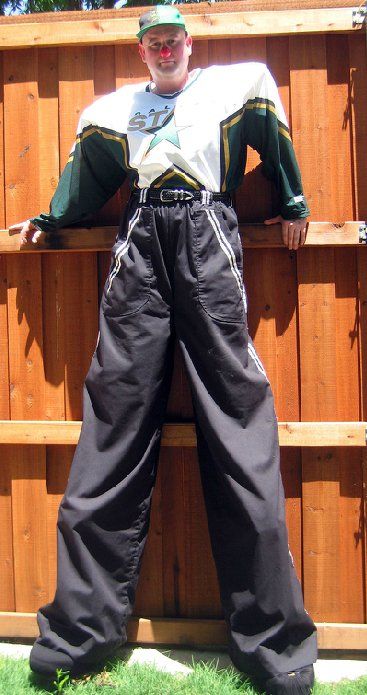 A man standing on stilts leaning against a wooden fence