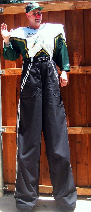 A man wearing stilts is standing in front of a wooden fence
