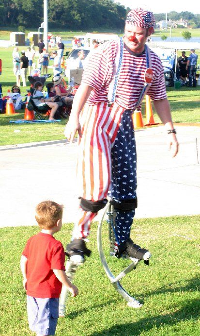 A clown on stilts is talking to a little boy