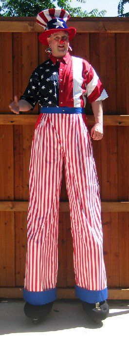 A man dressed as uncle sam on stilts is standing in front of a wooden fence