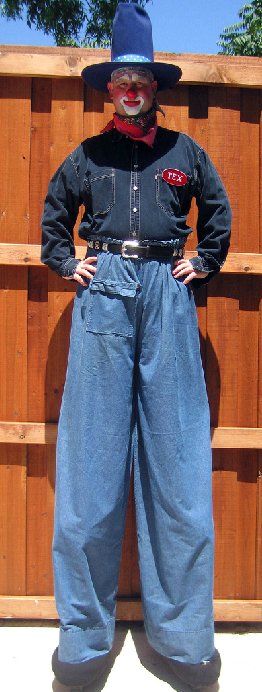A man in a cowboy outfit is standing in front of a wooden fence
