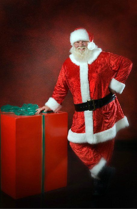A man dressed as santa claus standing next to a large red gift box