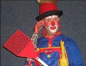 A clown is holding a red spatula and talking on a cell phone.