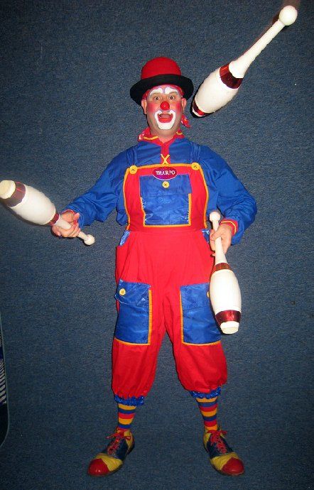 A clown in a red and blue outfit is juggling three clubs