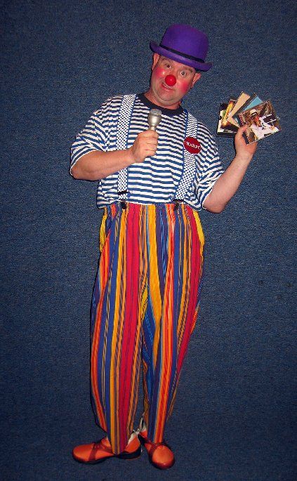 A man dressed as a clown is holding a microphone and cards