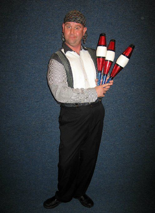 A man in a tuxedo is holding three juggling pins
