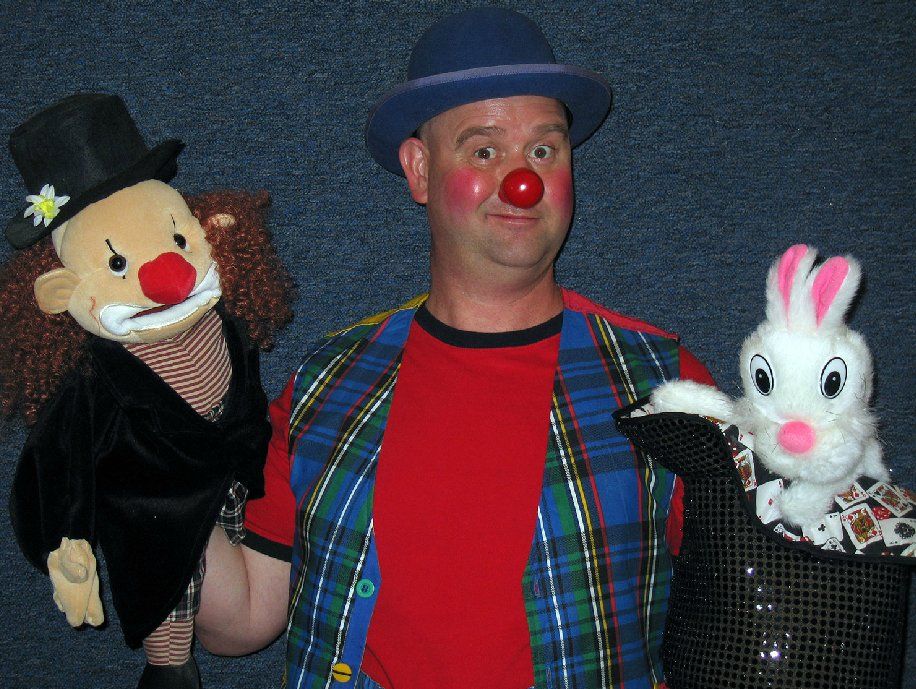 A man in a clown costume is holding a stuffed clown and a stuffed rabbit
