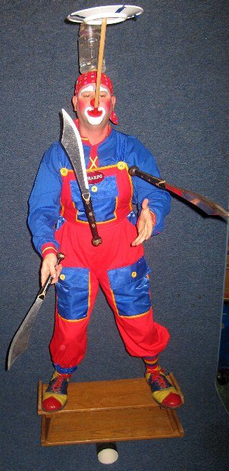 A clown is holding knives and a plate on his head