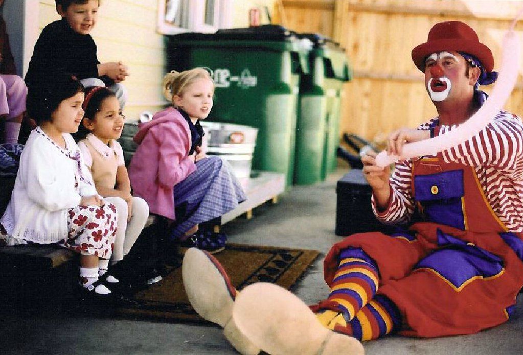 A clown is sitting on the ground playing with children