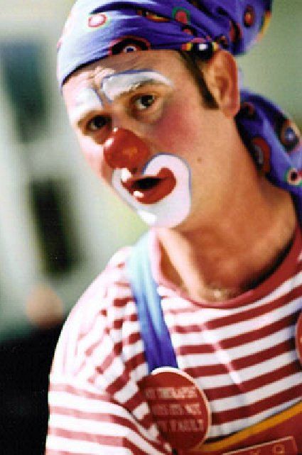 A close up of a clown wearing a striped shirt and a purple scarf