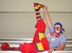 A clown is laying on a bench with his leg up