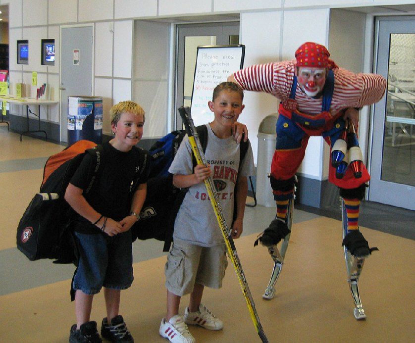 A boy wearing a shirt that says navy is standing next to a clown on stilts