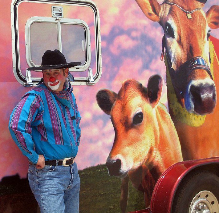A man with a clown nose is standing in front of a painting of cows