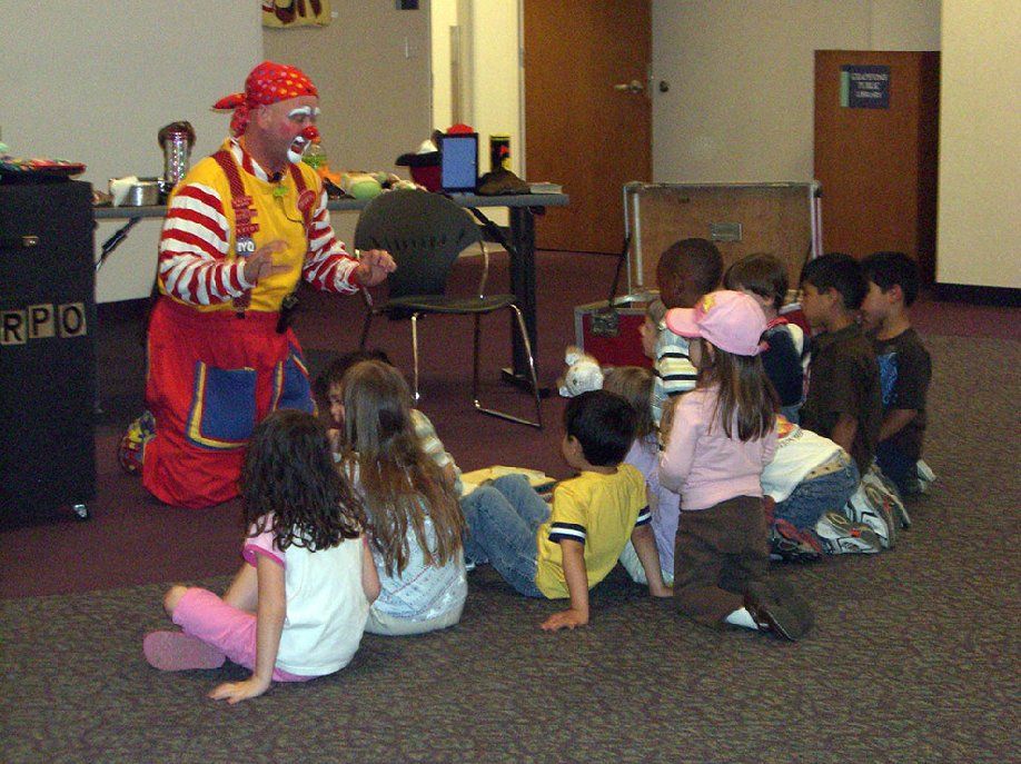 A group of children are sitting on the floor watching a clown perform