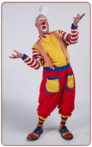 A clown in a yellow shirt and red pants is juggling a ball