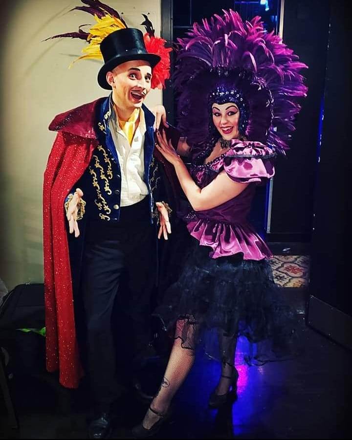 A man in a top hat stands next to a woman in a purple dress