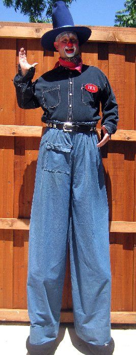A clown on stilts wearing a cowboy hat and blue jeans