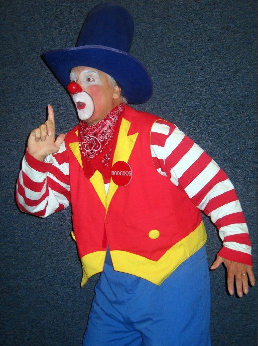 A clown wearing a blue hat and striped sleeves is pointing up