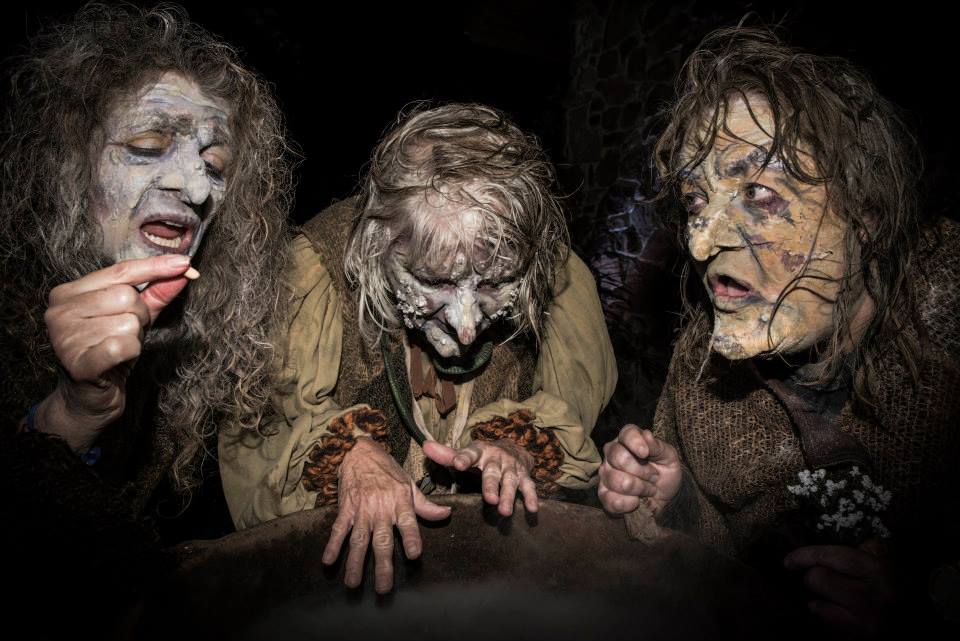 Three witches are standing next to each other in a dark room.