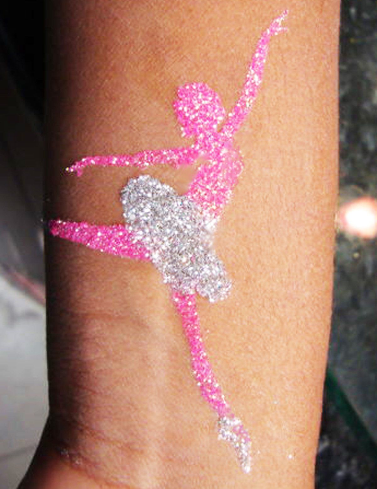 A person has a pink and silver ballerina tattoo on their arm
