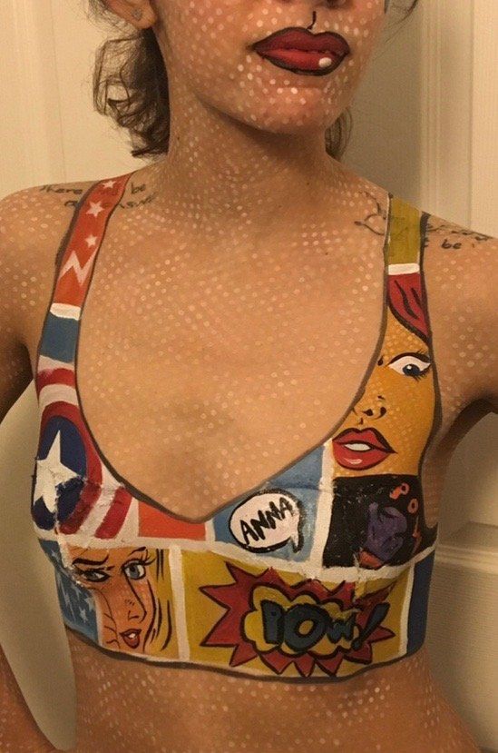 A woman is wearing a crop top with comic book characters painted on it.