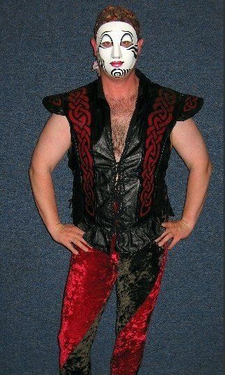 A man wearing a white mask and a black vest is standing with his hands on his hips.