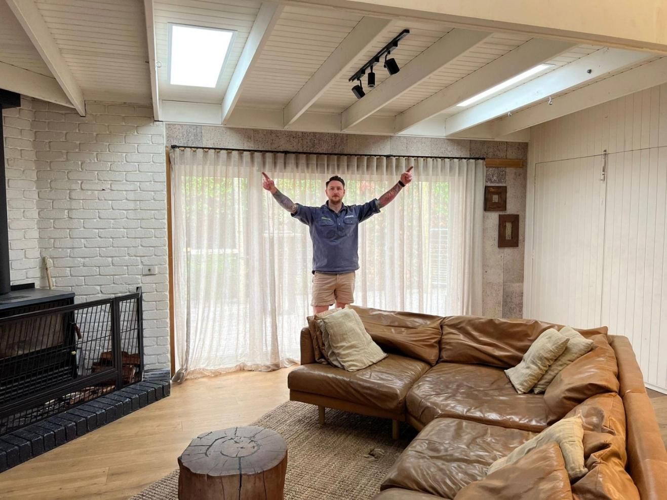 A Man Is Standing In A Living Room With His Arms Outstretched — The Woolmen In Murwillumbah, NSW